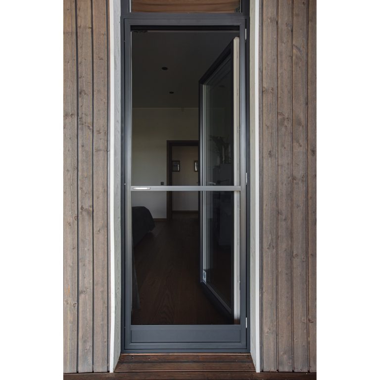 En Myggnät dörr - öppningsbar med en mörk metallram är placerad i en trävägg och visar det inre rummet genom sitt glas.